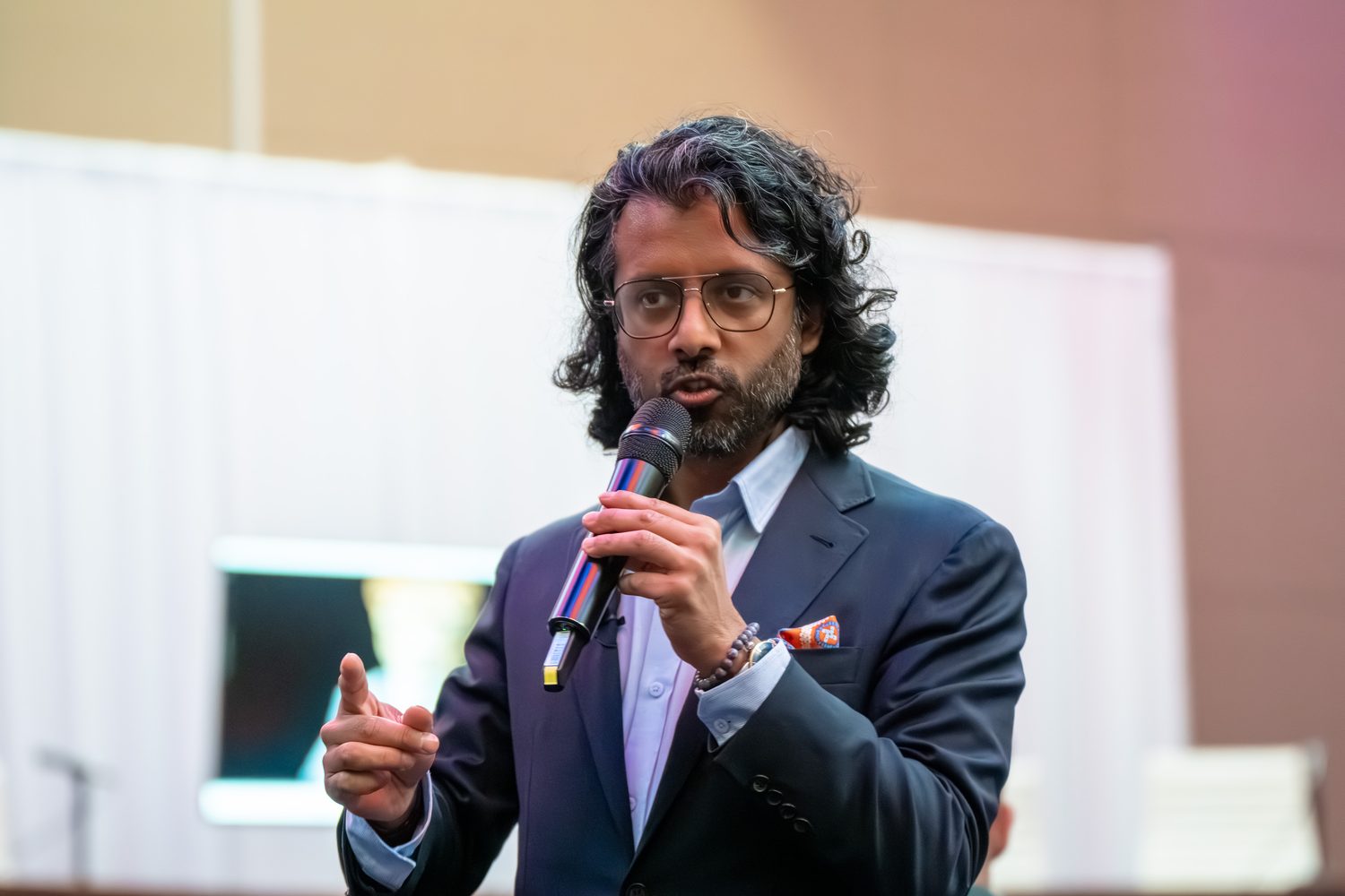 Conference speaker addressing the room mid-sentence, microphone in hand