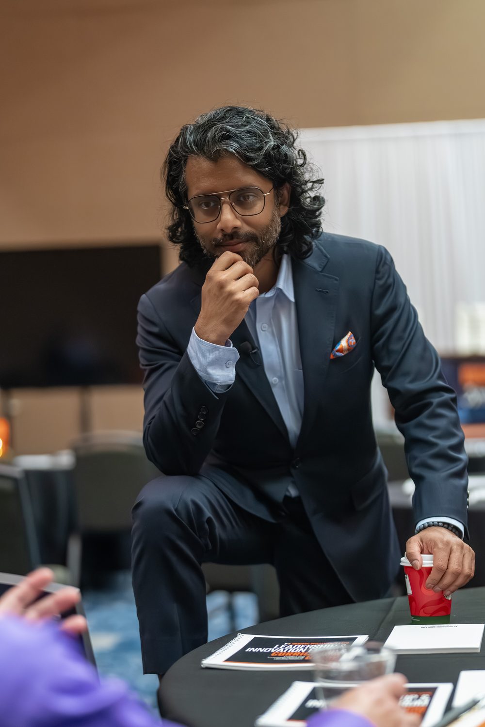 Speaker seated on a table edge with coffee during a break
