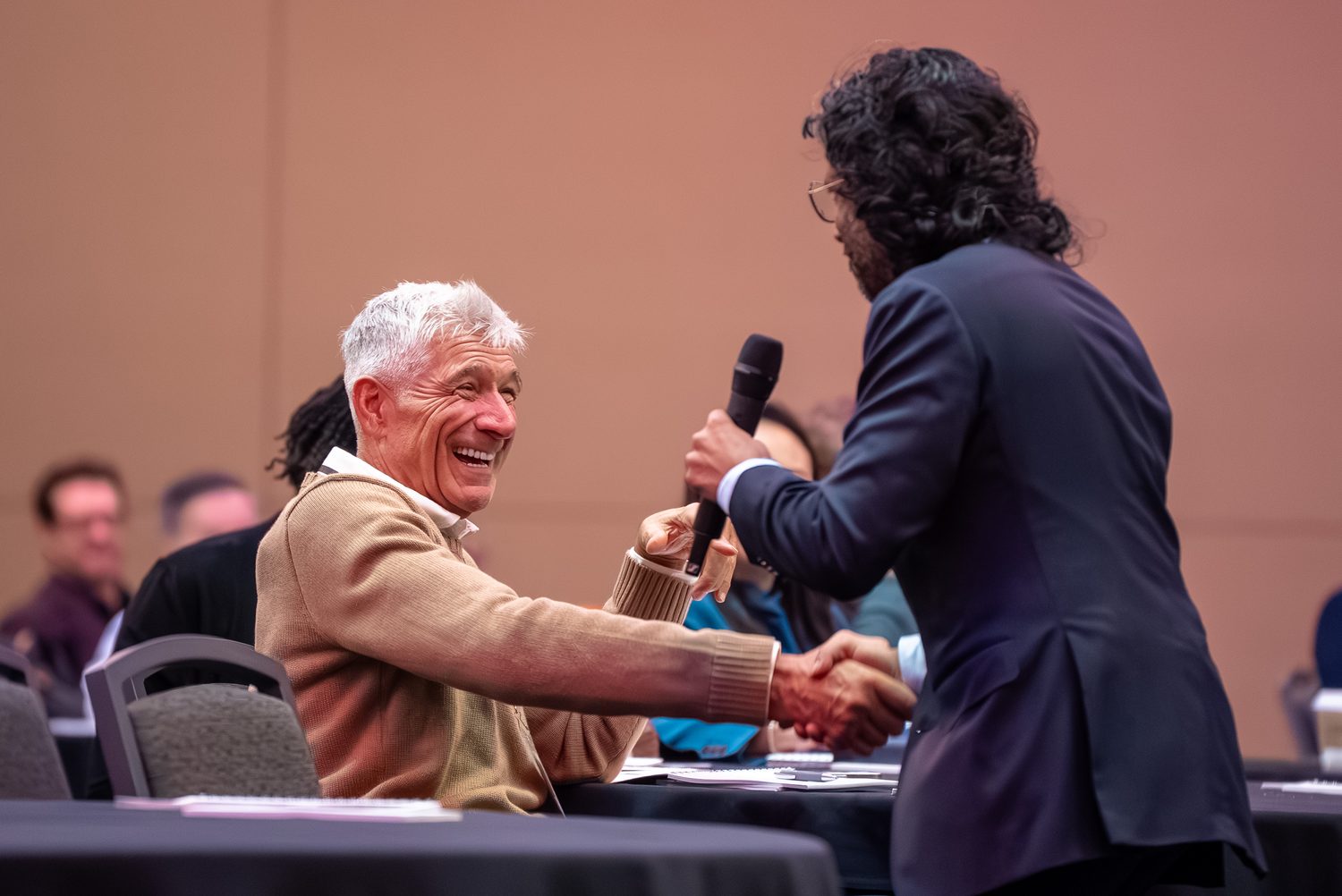 Speaker sharing a laugh and a handshake with a seated attendee