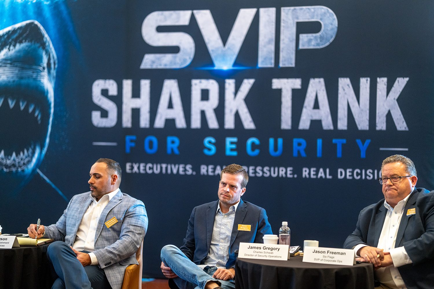 Three executive judges seated before the SVIP Shark Tank for Security backdrop